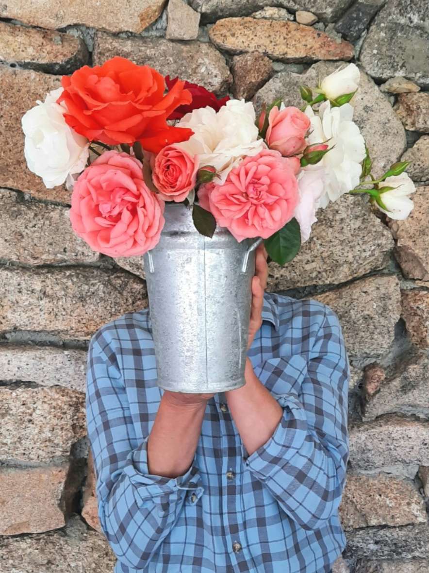 Someone holding a zinc bucket of roses in front of their face, against a stone wall