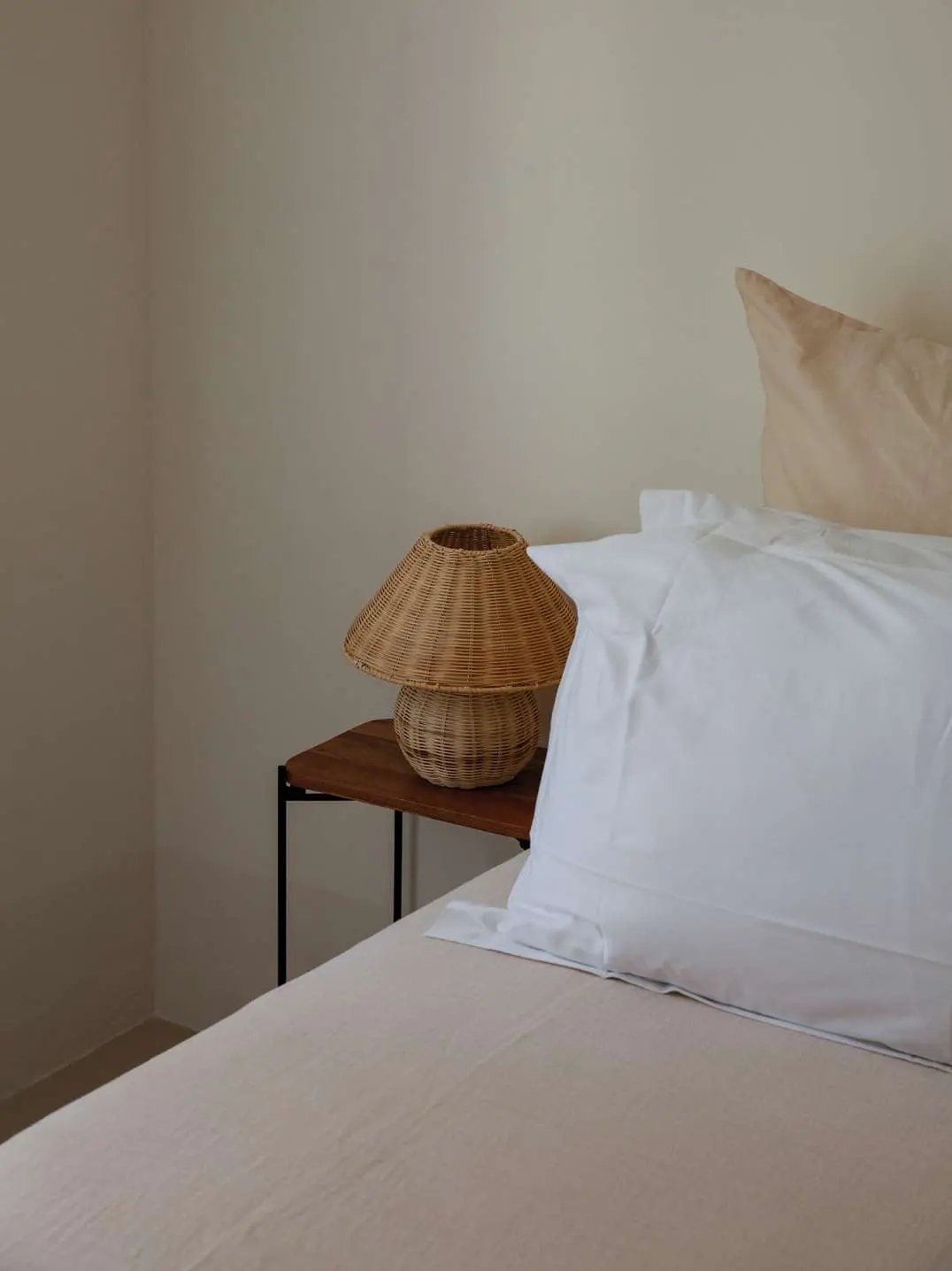 A bed made up in white linen, a woven rattan lamp on the bedside table