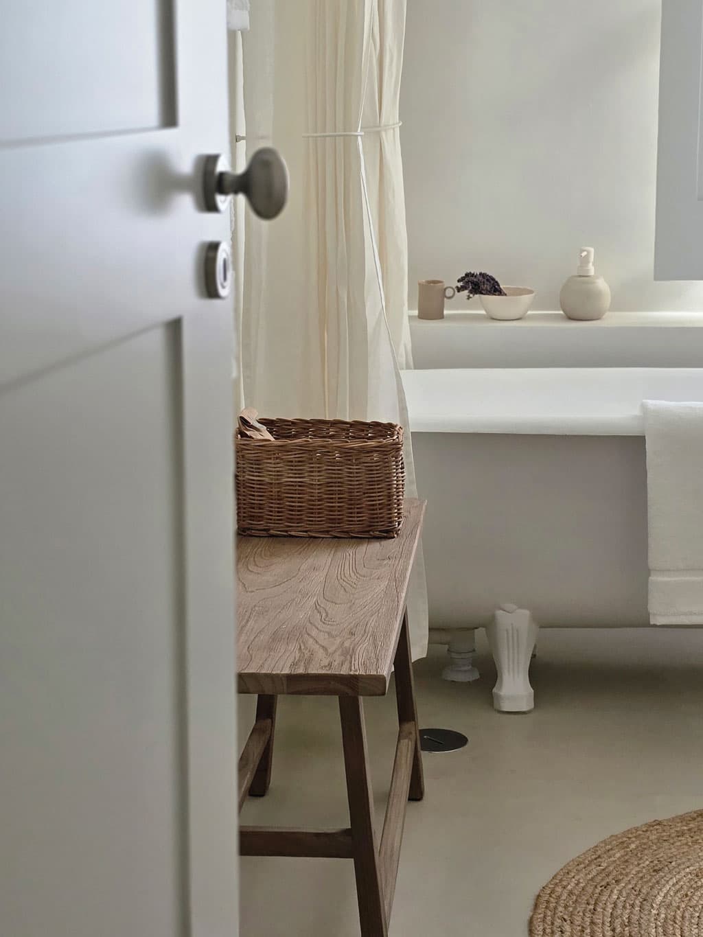 A bathroom glimpsed through a half-open door, a basket on the bench