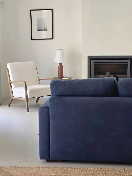 A sitting room with a deep blue sofa, a linen armchair and a wood-burning stove