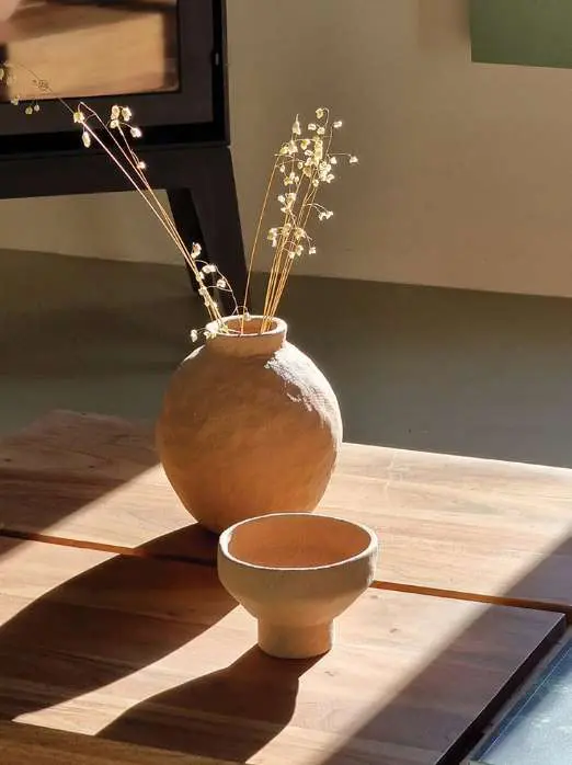 A round terracotta vase of dried flowers and a small bowl on a sunlit table
