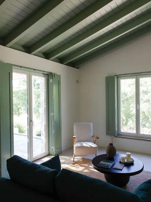 A sitting room under green-painted beams, a deep green sofa facing the open doors