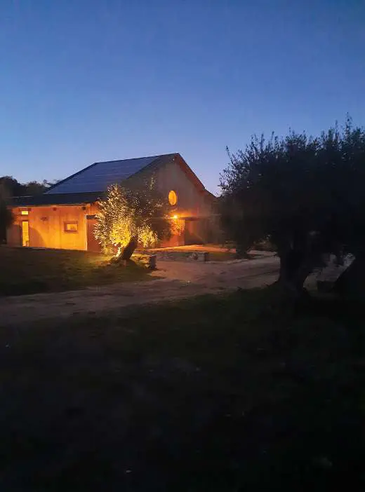 The barn lit from within at dusk, its windows warm against a deep blue sky