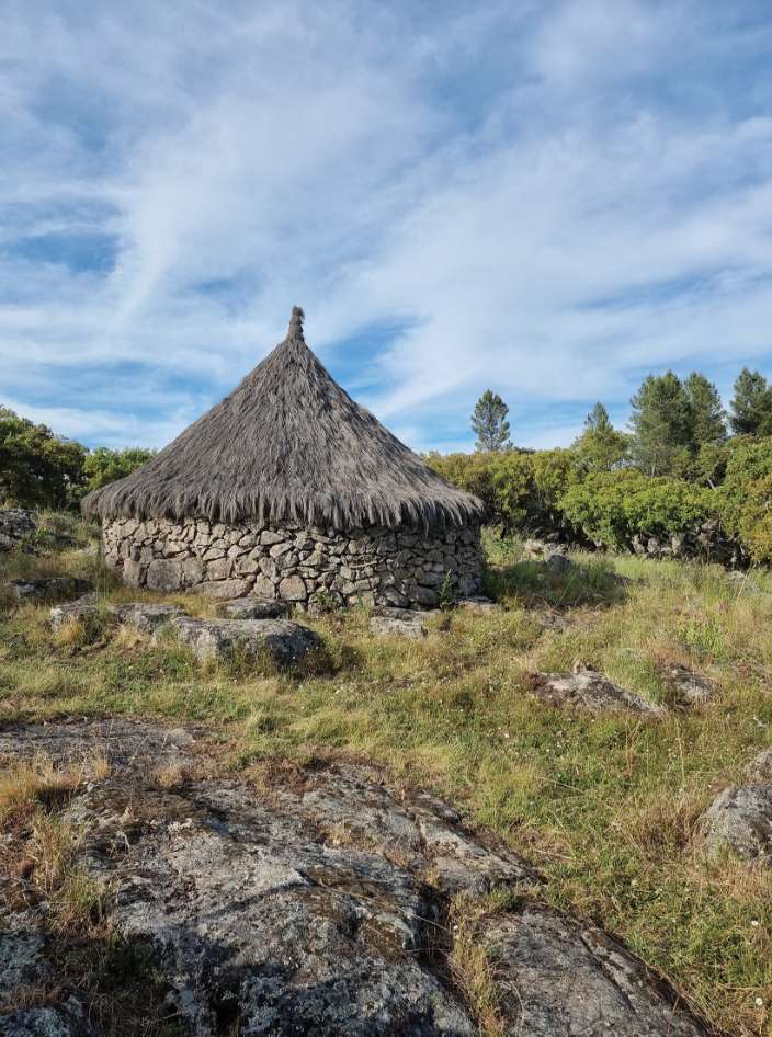 A round stone hut with a thatched roof standing among granite boulders